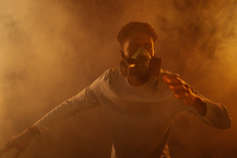 A man wearing a gas mask stands amid thick smoke, evoking themes of air pollution and climate change.