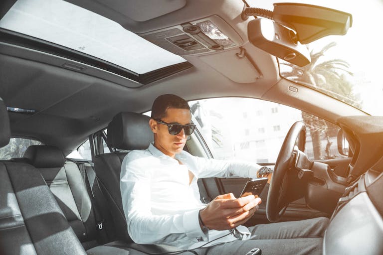 A man wearing sunglasses texts on his phone while driving a car in Morocco.