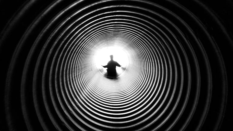 A person silhouetted against light at the end of a spiral tunnel, creating a striking black and white contrast.