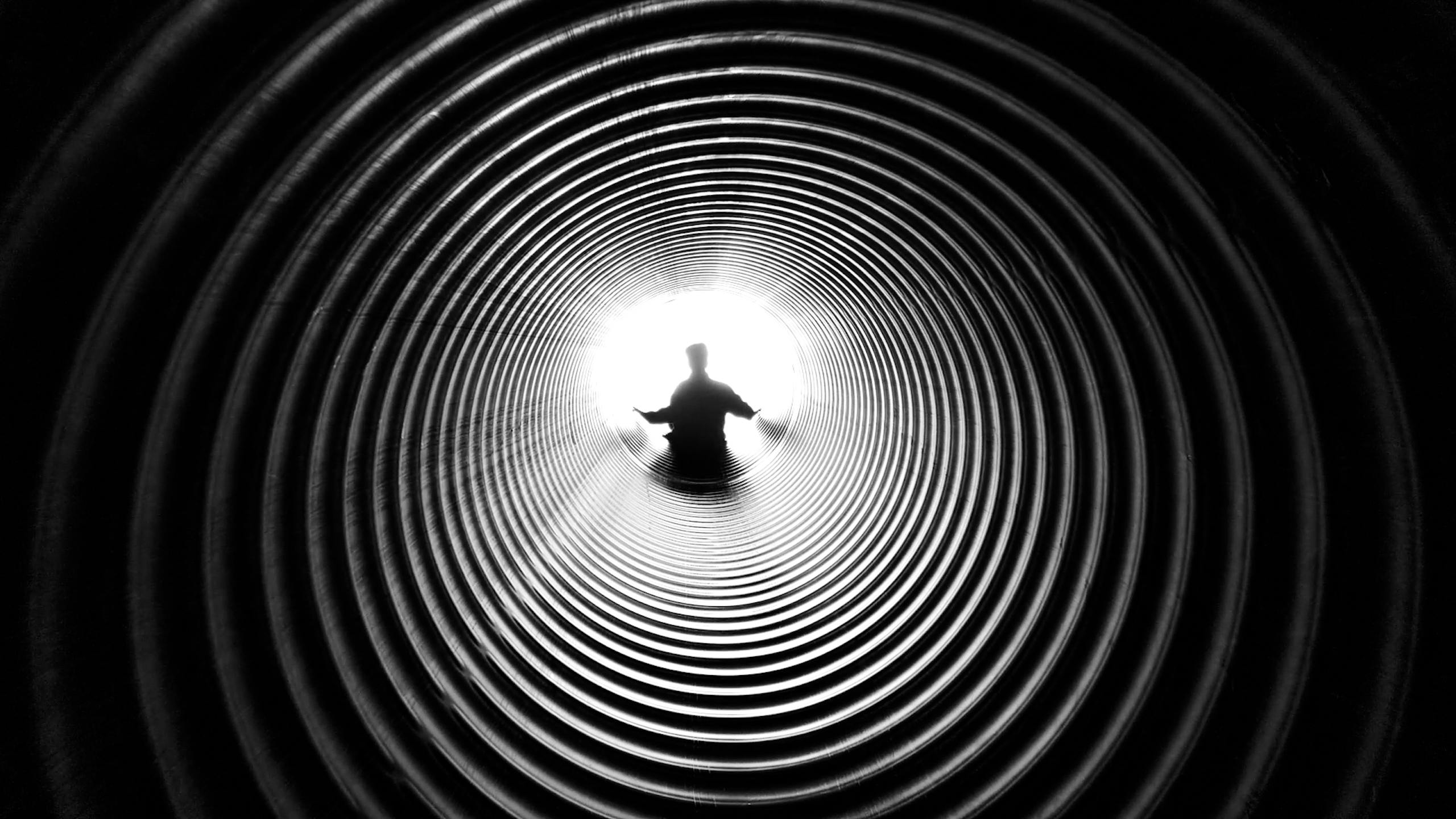 A person silhouetted against light at the end of a spiral tunnel, creating a striking black and white contrast.