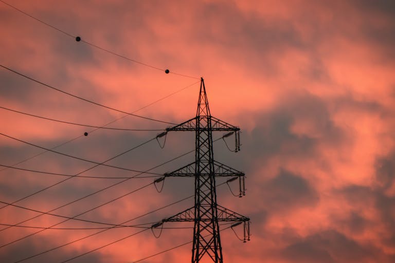 A striking silhouette of an electricity pylon against a vibrant sunset sky.