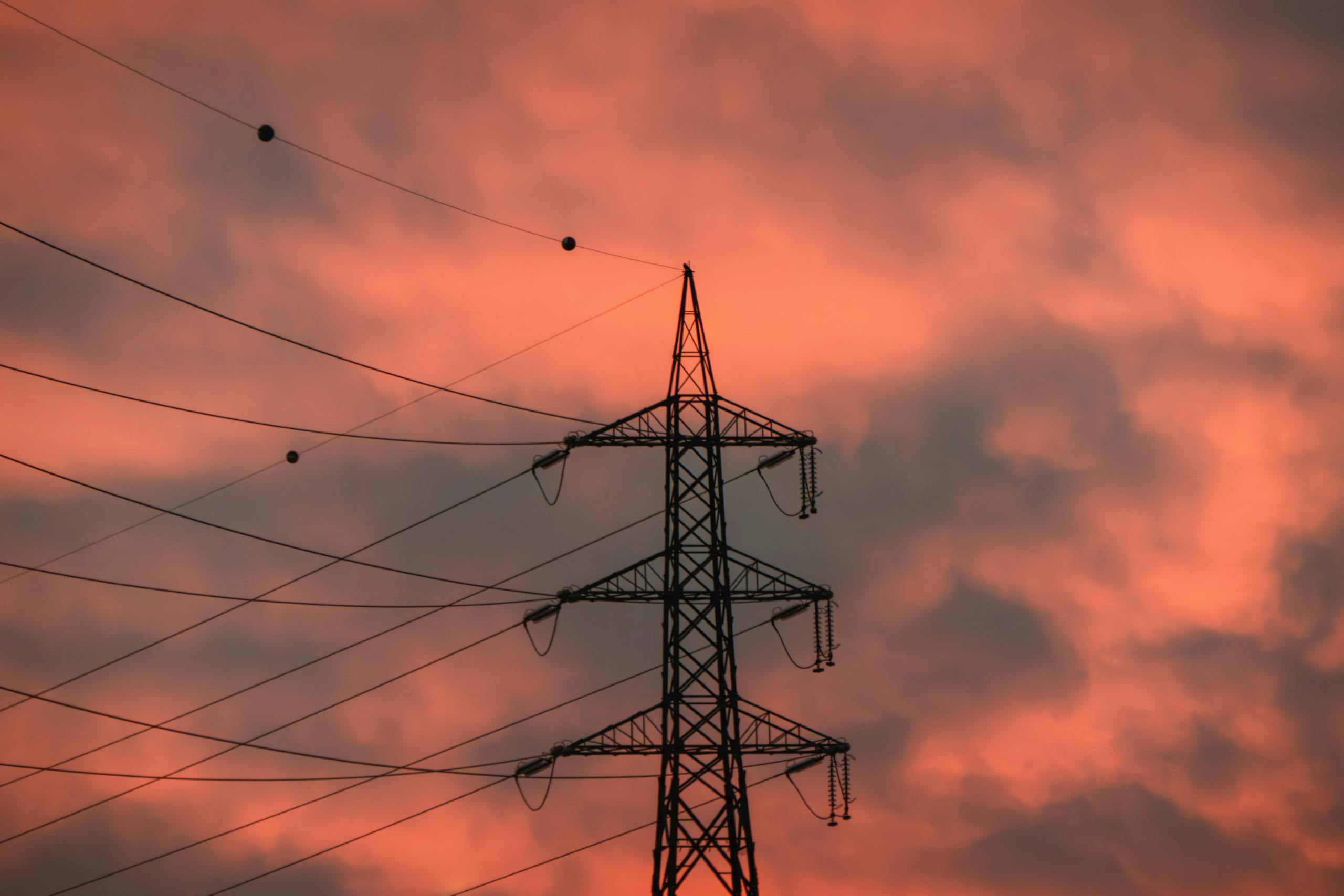 A striking silhouette of an electricity pylon against a vibrant sunset sky.