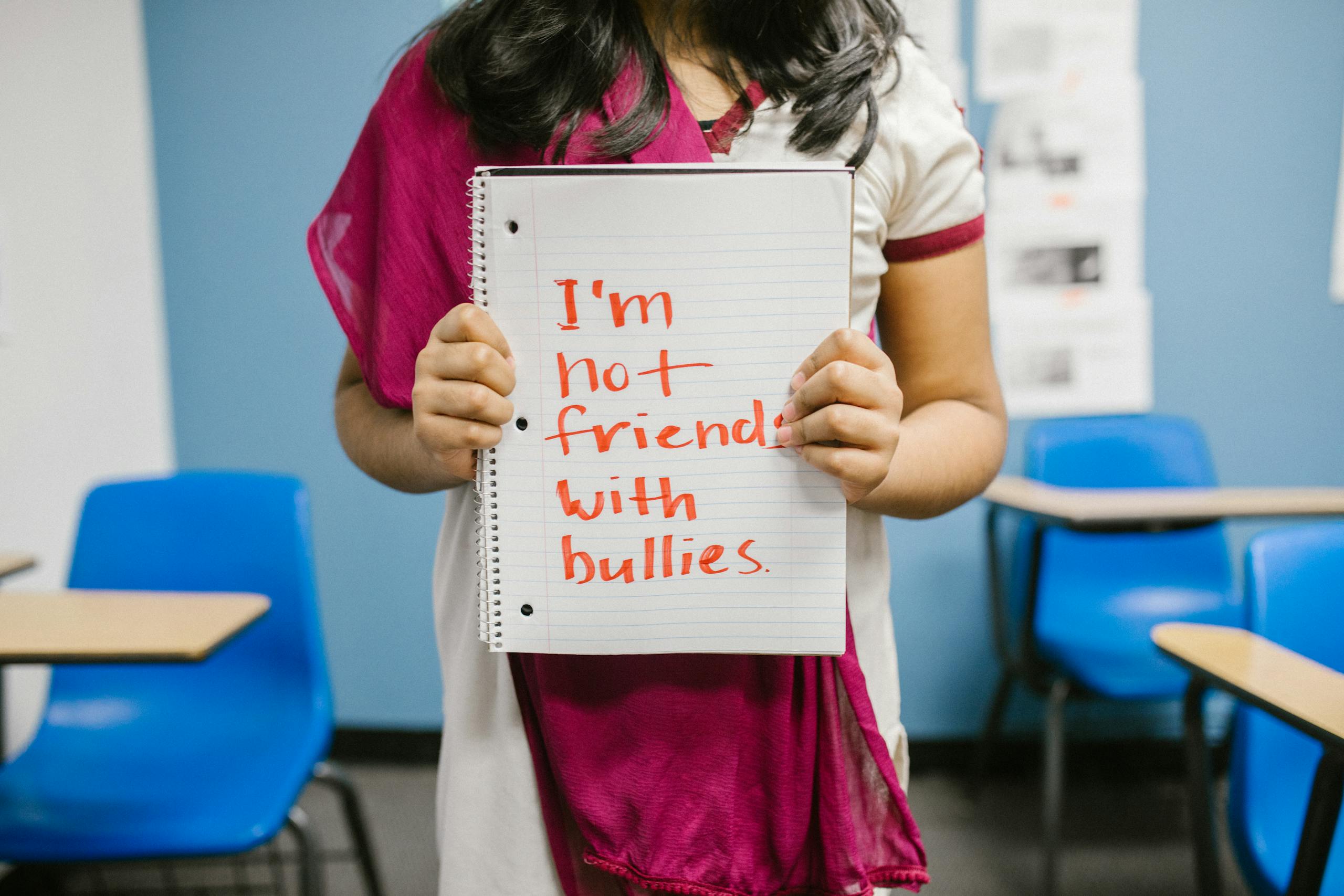 A student in a classroom holds a notebook with an anti-bullying message.