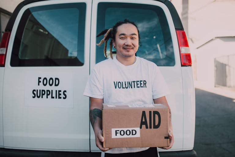 A volunteer holding a box of food aid in front of a supply vehicle, symbolizing generosity and help.