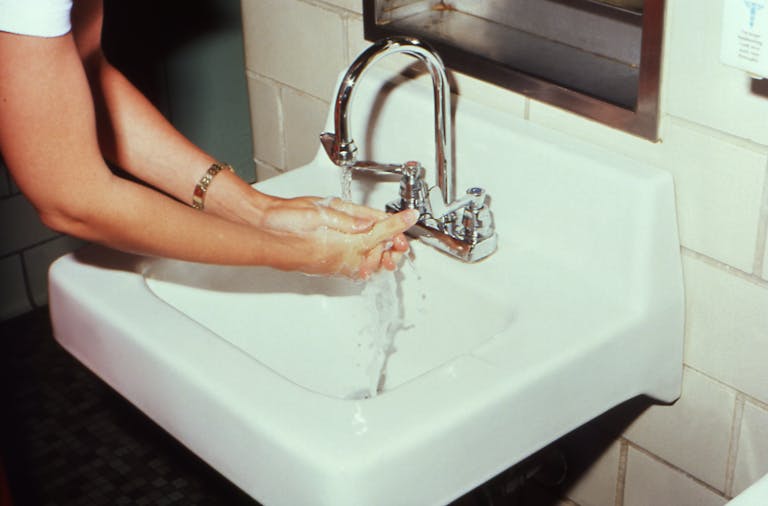 A woman washing hands at a bathroom sink, highlighting hygiene and cleanliness.