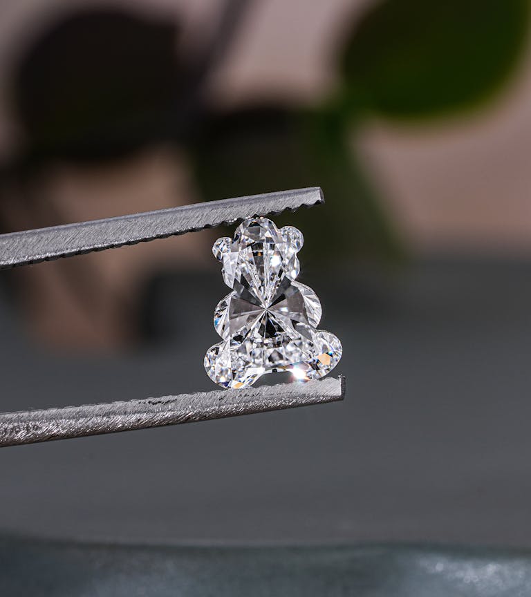Close-up of a teddy bear shaped diamond held with tweezers, showcasing brilliance and craftsmanship.