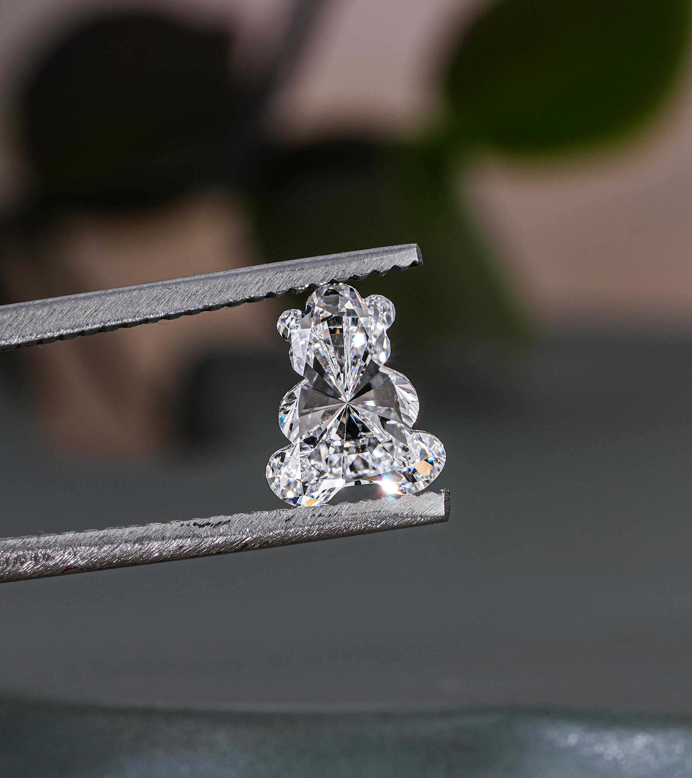 Close-up of a teddy bear shaped diamond held with tweezers, showcasing brilliance and craftsmanship.