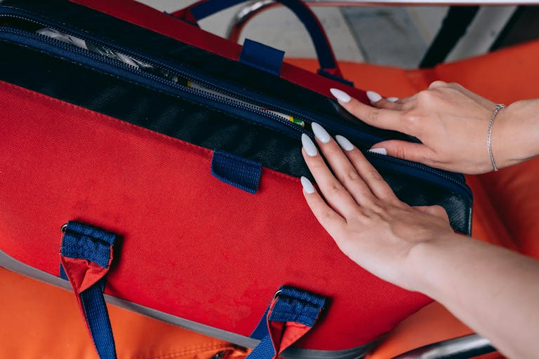 Close-up of a woman's hands opening a red medical bag, highlighting emergency preparedness.