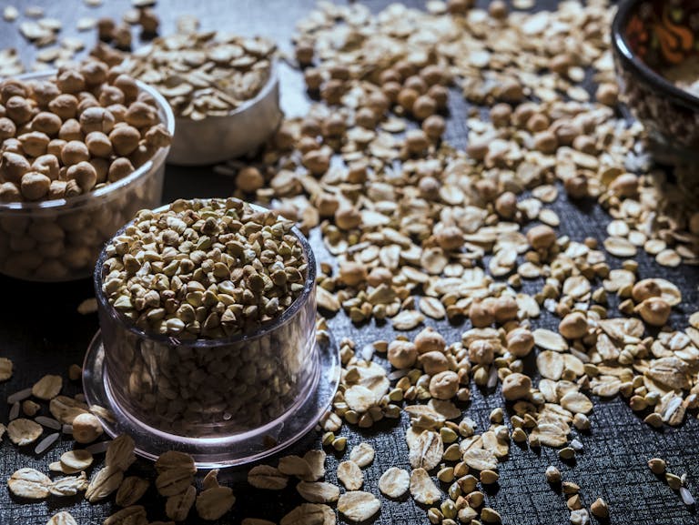 Close-up of diverse grains and legumes in plastic cups on a textured surface, highlighting healthy food options.
