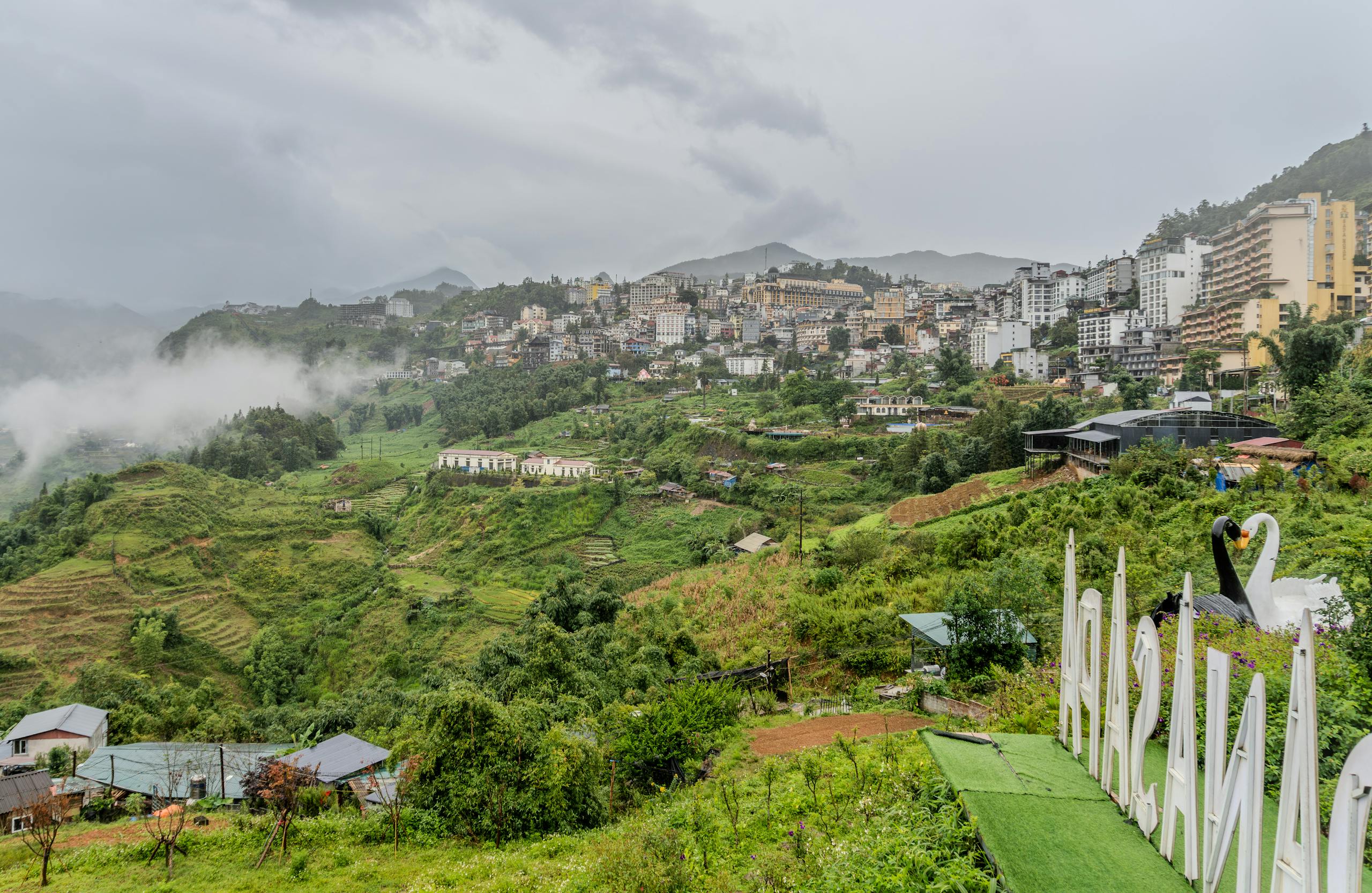 Explore a scenic view of a mountain cityscape with lush greenery and misty hills.