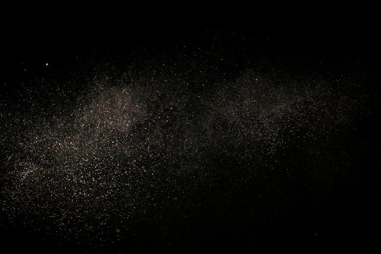 Fine dust particles suspended in air against a black backdrop, creating an abstract cosmic effect.