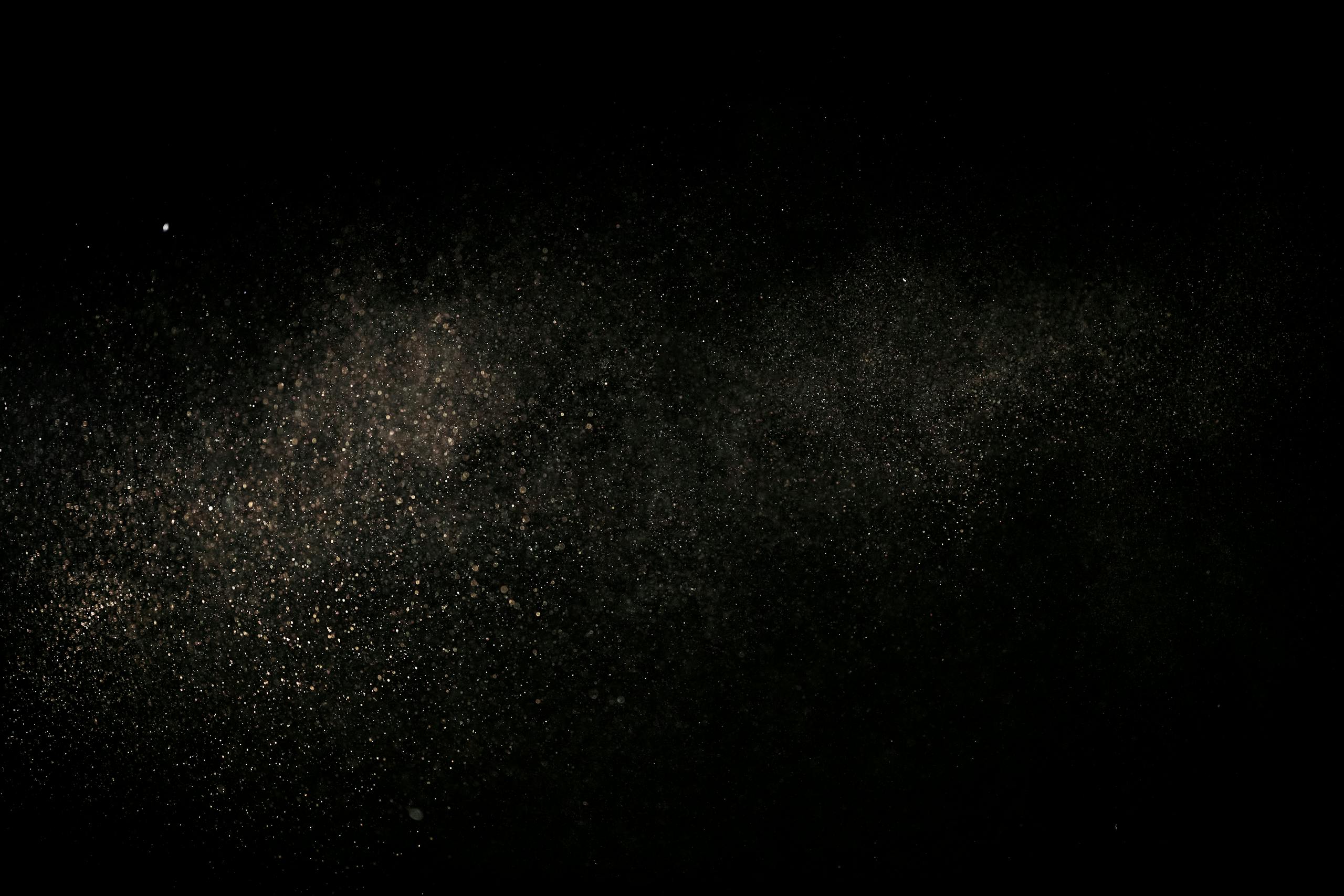 Fine dust particles suspended in air against a black backdrop, creating an abstract cosmic effect.