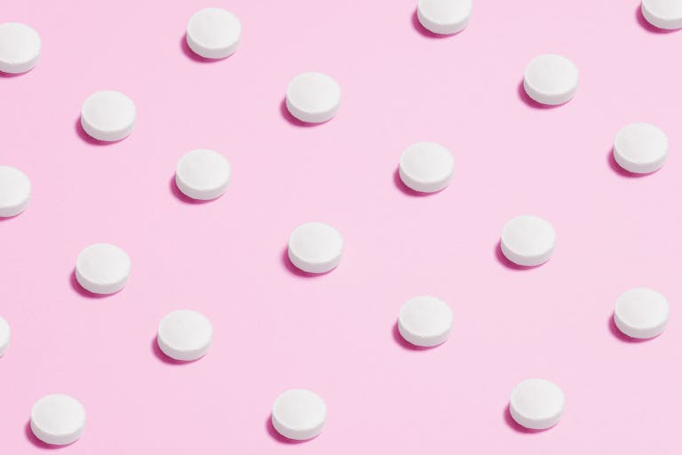 Flat lay of white pills on a pastel pink surface, showcasing a medical theme.