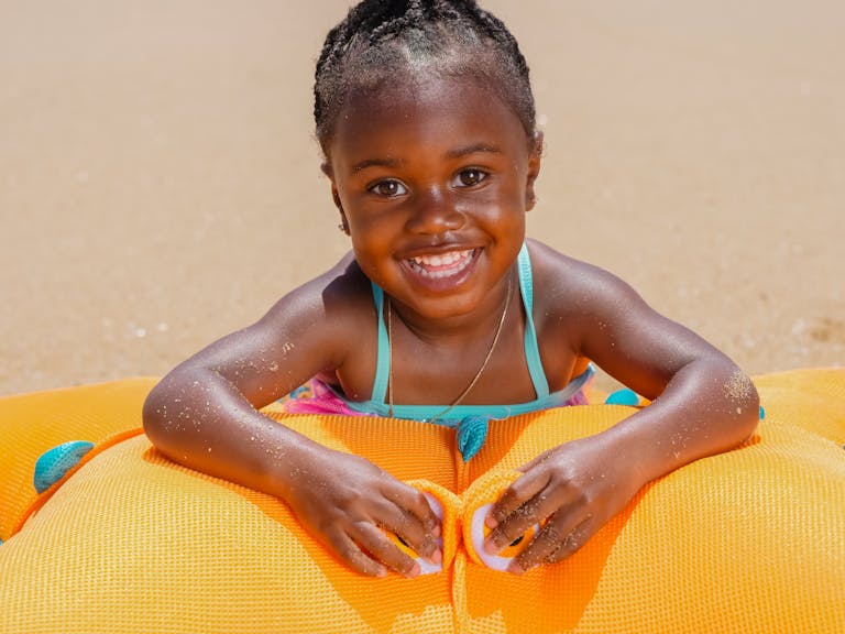 Happy young girl smiling on the beach, playing with an orange inflatable toy. Perfect summer fun.