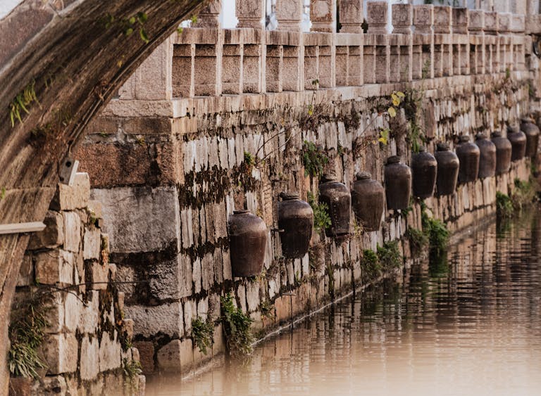 Old clay jugs line a stone wall beside a canal, showcasing rustic charm and historical ambiance.