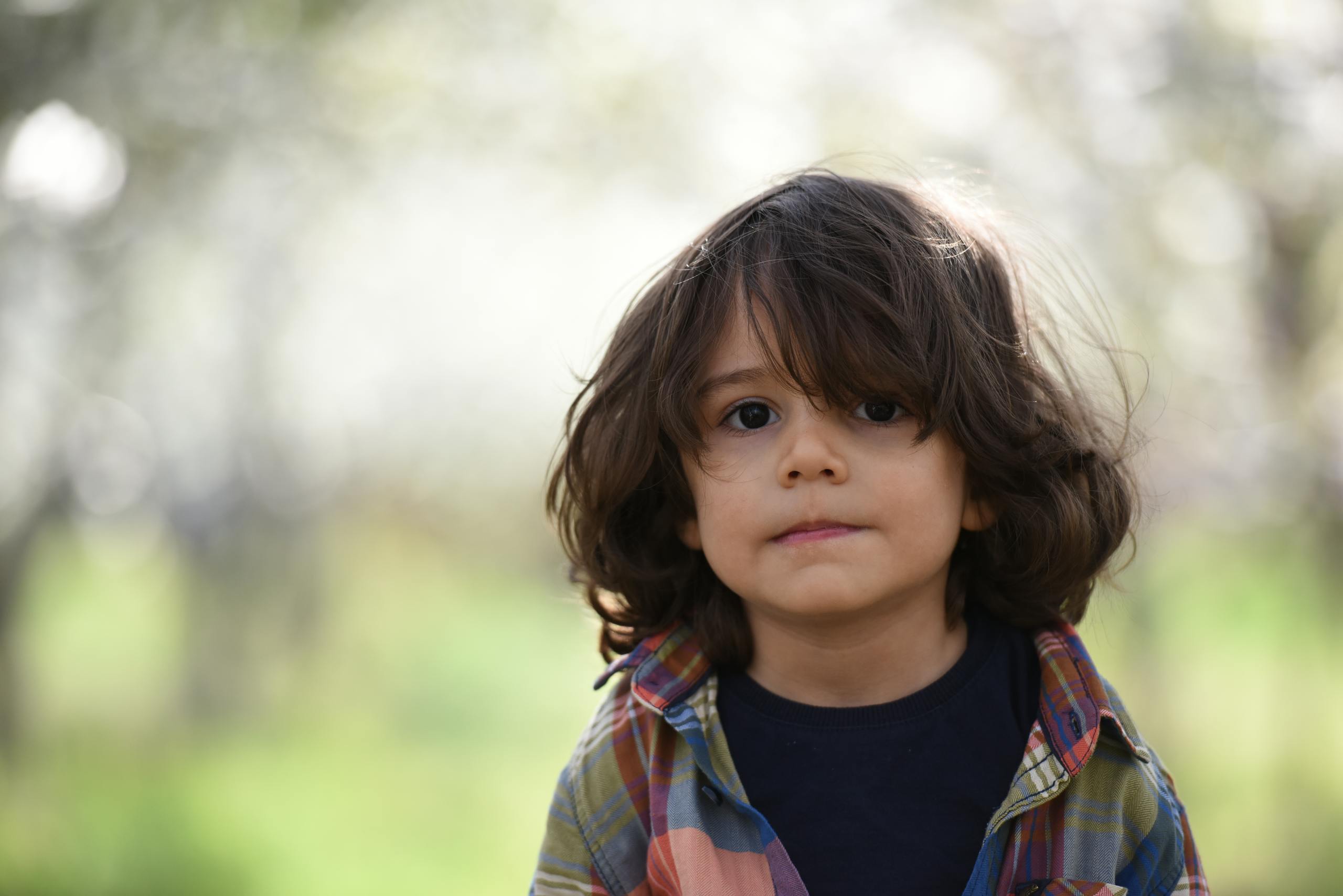 Portrait of a cute child with long hair wearing a plaid shirt, standing outdoors during spring.