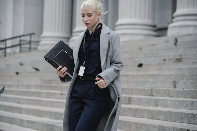 Professional woman in formal attire walking down courthouse steps holding folders outdoors.