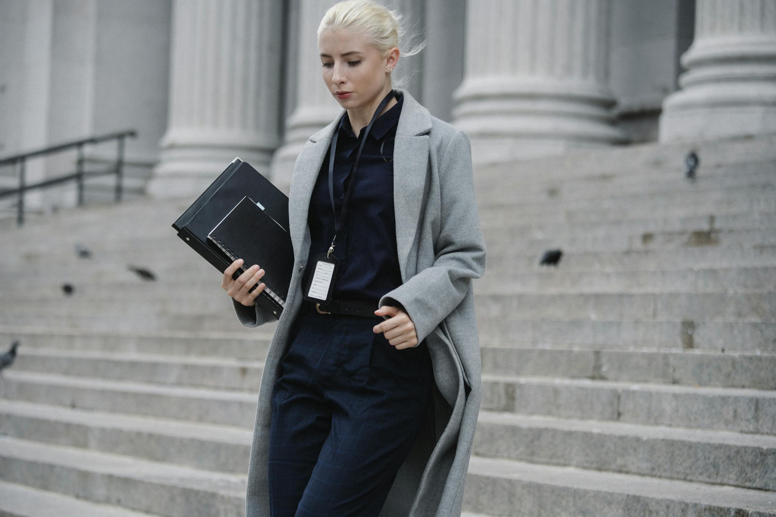 Professional woman in formal attire walking down courthouse steps holding folders outdoors.