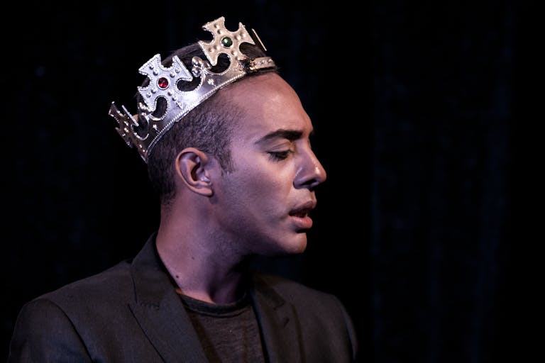 Profile portrait of a man wearing a crown, captured in dramatic stage lighting, evoking theatrical elegance.