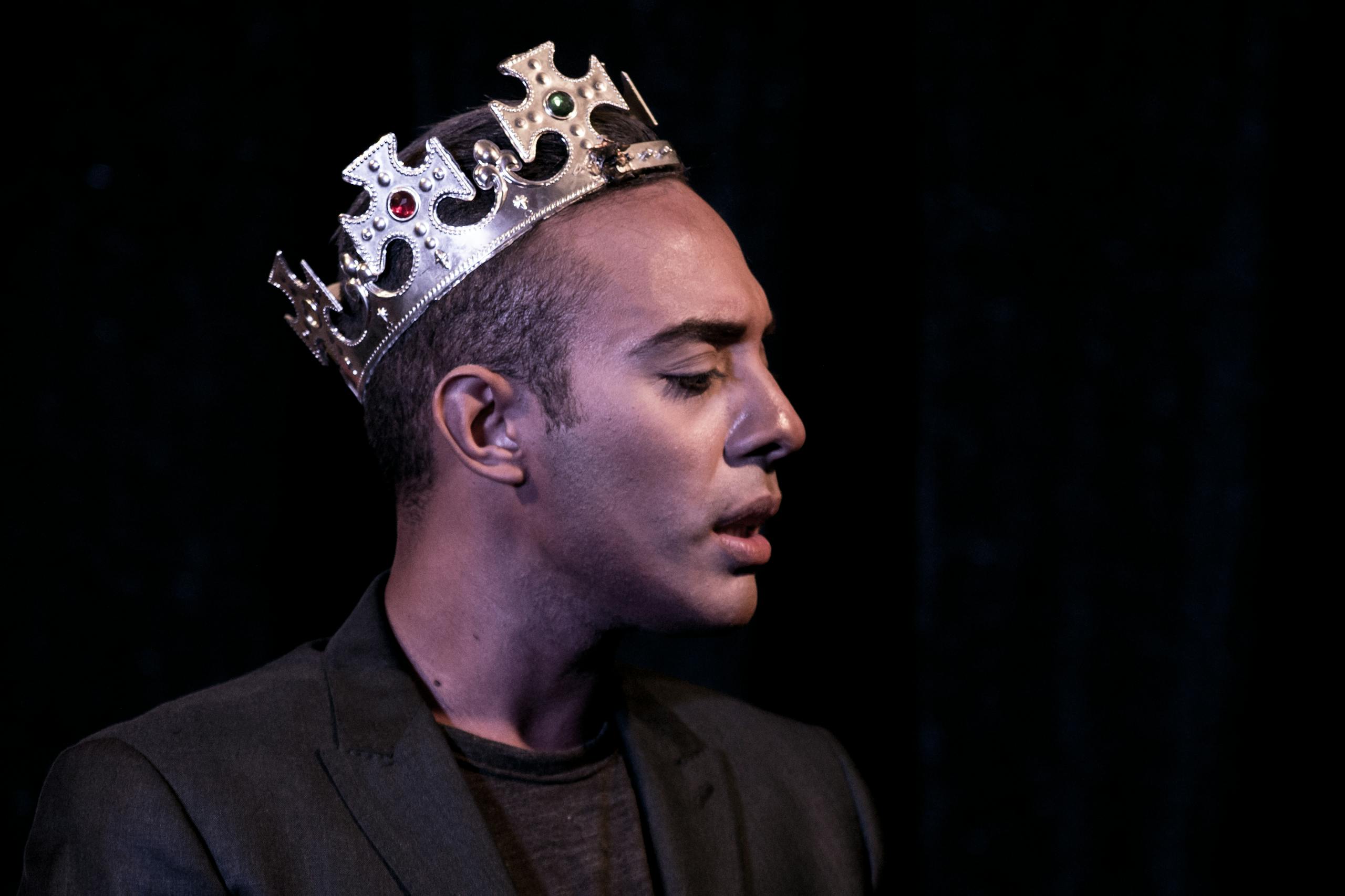 Profile portrait of a man wearing a crown, captured in dramatic stage lighting, evoking theatrical elegance.