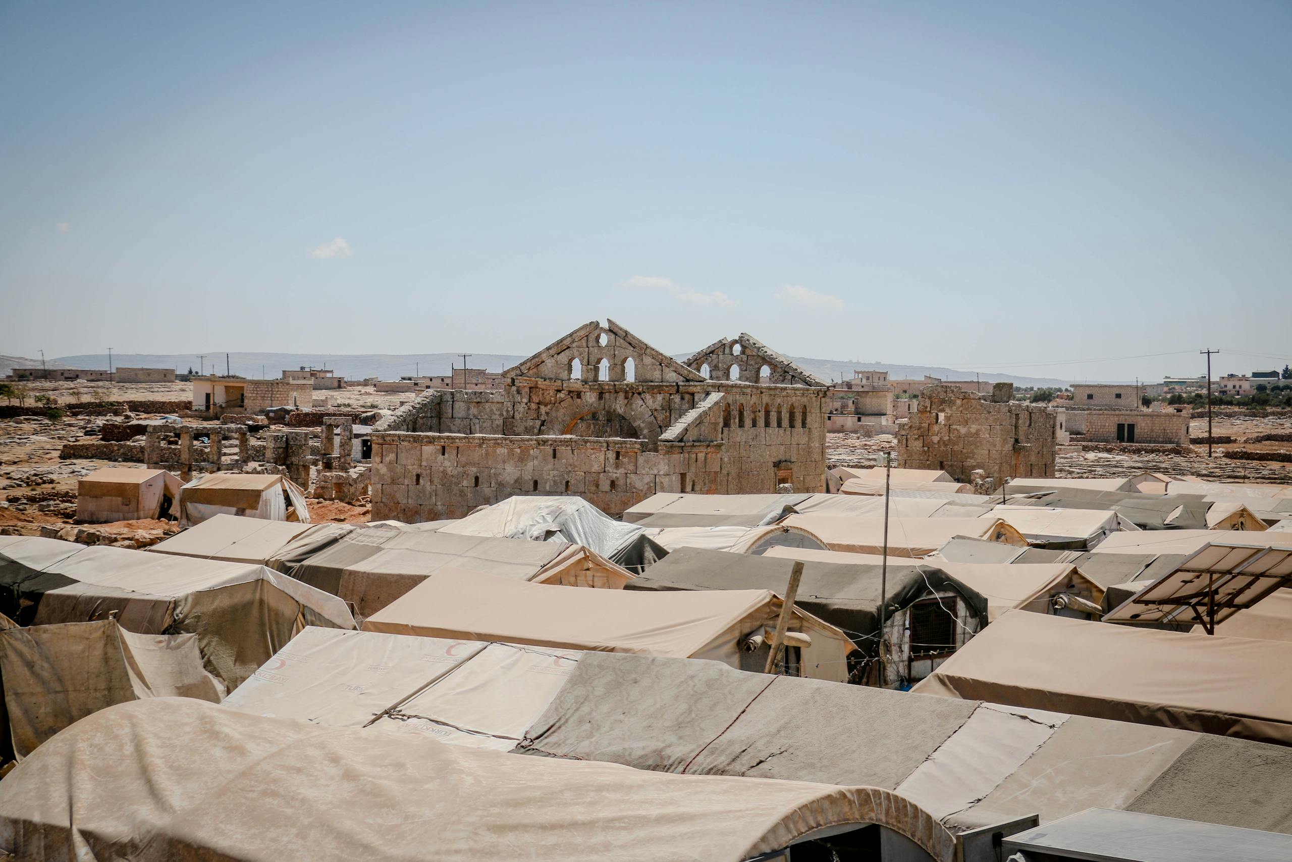 Ruins and temporary shelters in Idlib, Syria under a clear sky.