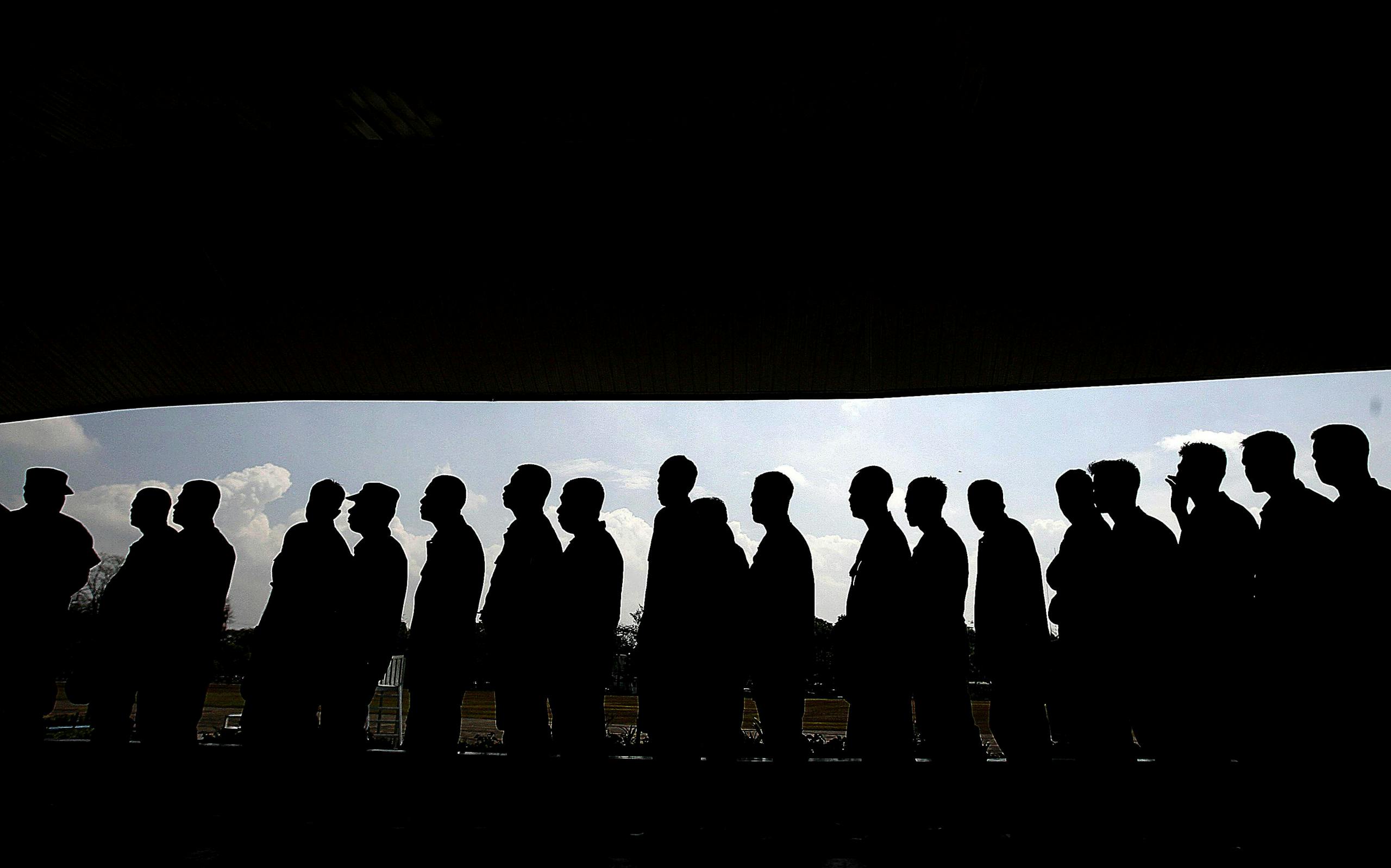 Silhouettes of people in line under a shaded canopy, highlighting social interaction and society.