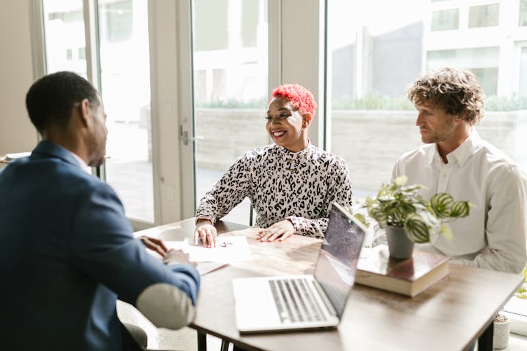Three professionals meeting in a sunny office discussing finance with smiles.