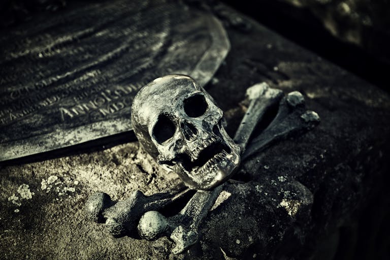 A haunting close-up of a skull and crossbones on an ancient tombstone in a spooky cemetery.