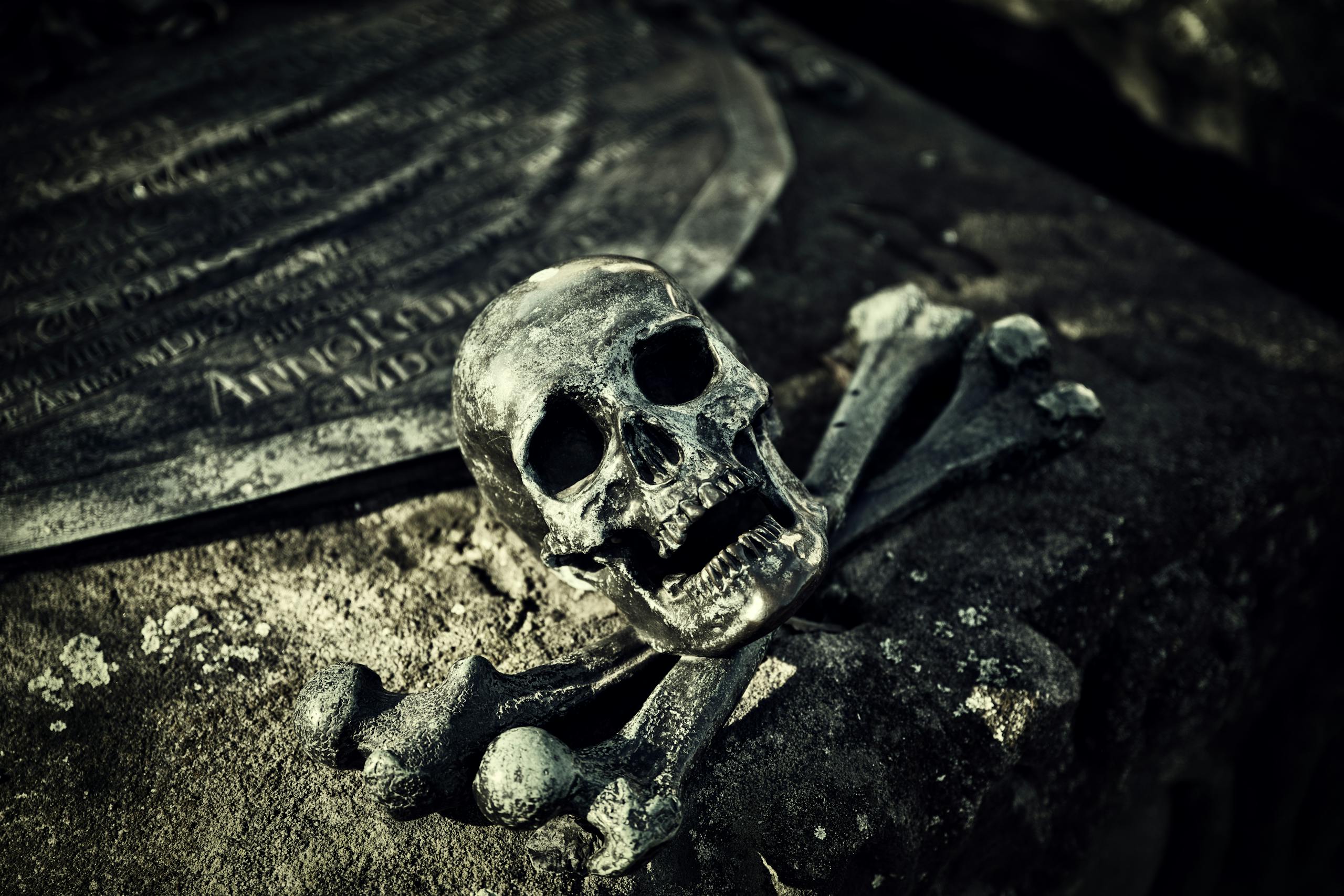 A haunting close-up of a skull and crossbones on an ancient tombstone in a spooky cemetery.