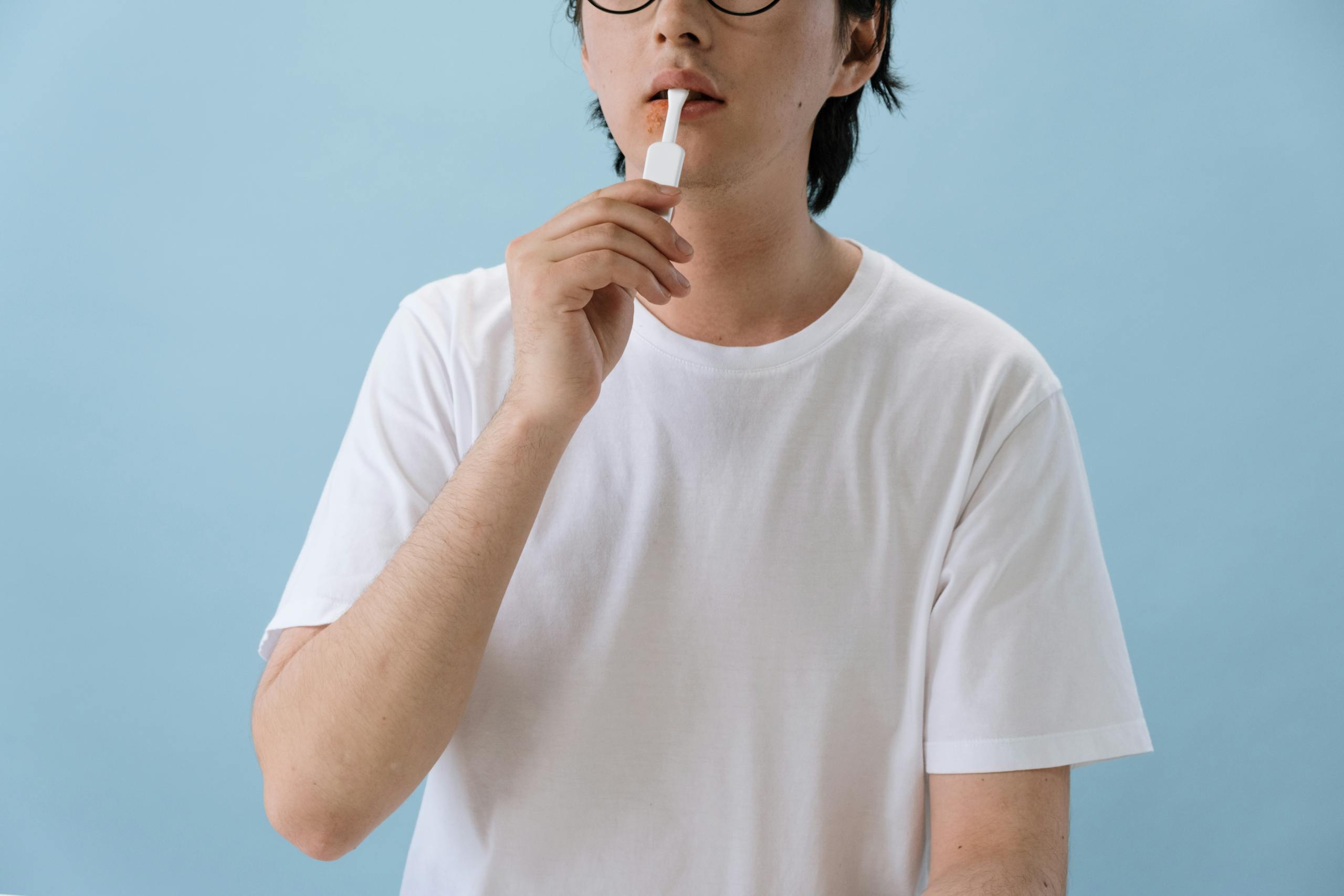A person in white T-shirt using an oral swab test kit indoors with a blue background.