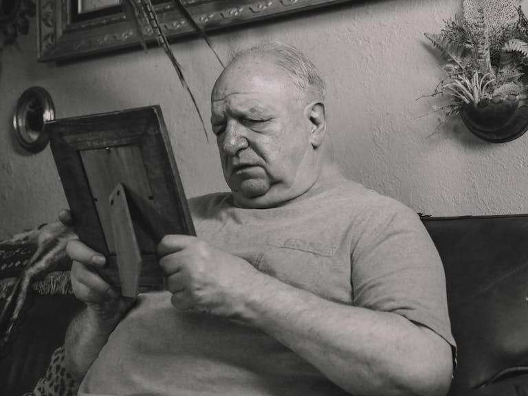 A senior man holding a wooden frame, lost in deep thought and emotion.
