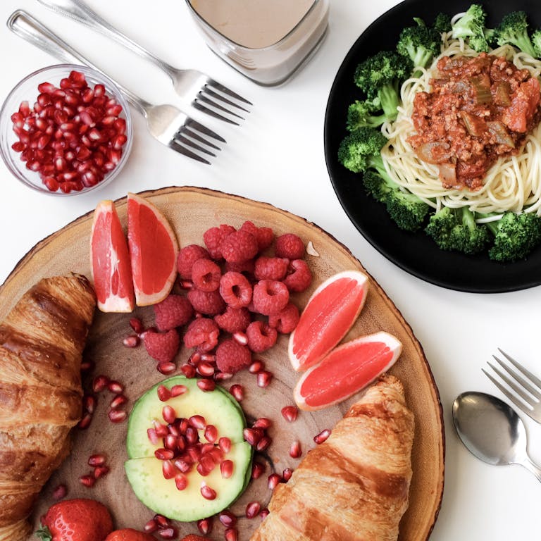 A vibrant breakfast spread with croissants, pasta, and fresh fruits, perfect for food lovers.