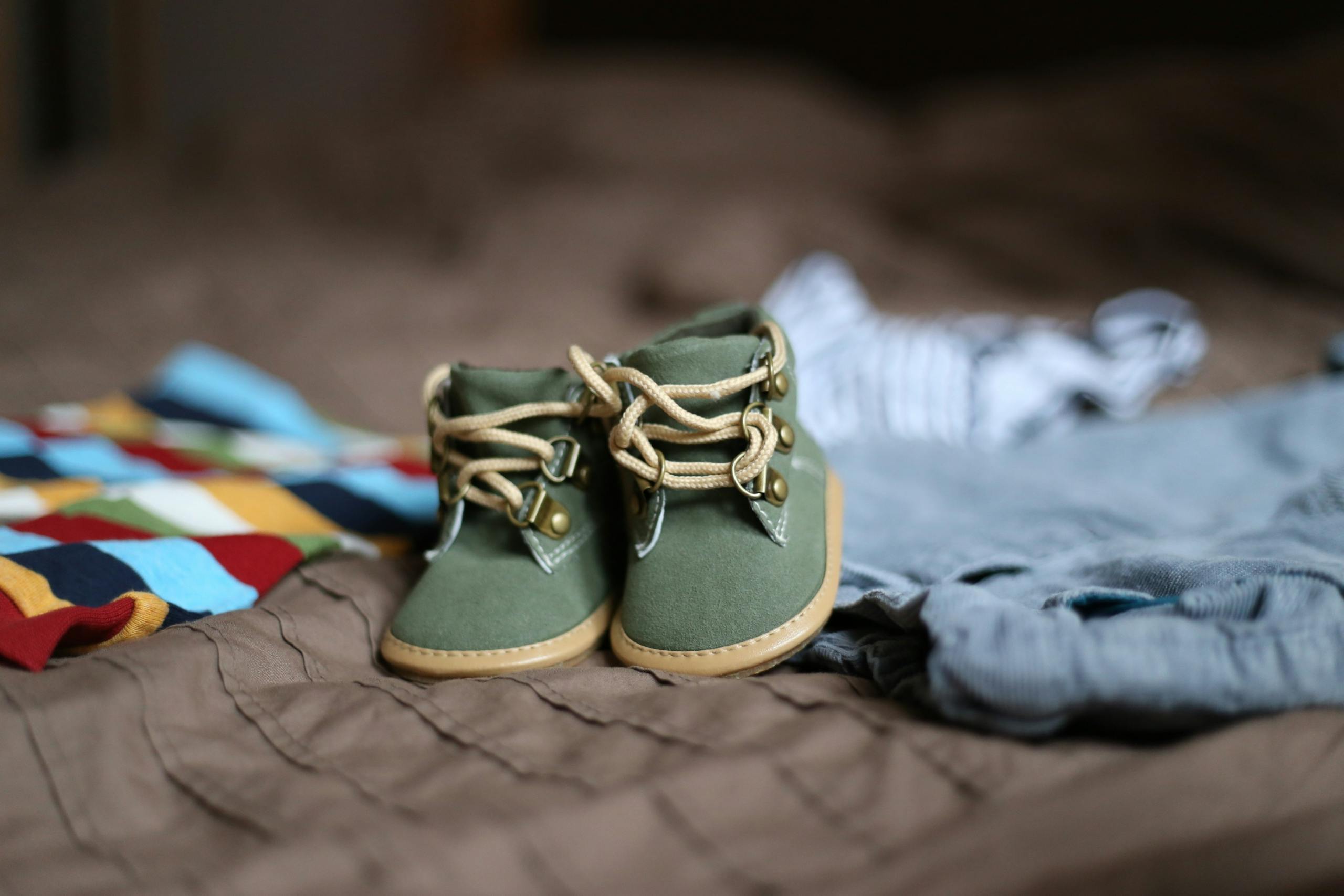Adorable green baby booties surrounded by colorful clothes, perfect for infant fashion.