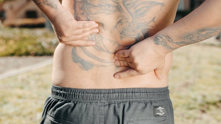 Close-up of a man holding his tattooed back outdoors, possibly experiencing back pain.
