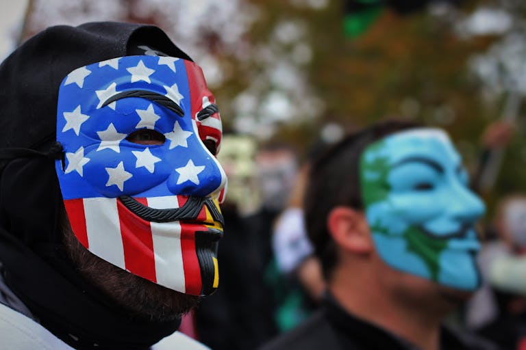 Close-up of protesters wearing Guy Fawkes masks with political themes, highlighting activism.