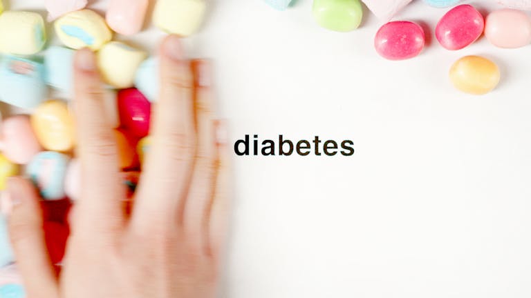 Conceptual image of a hand moving candies away from the word 'diabetes' on a white background.