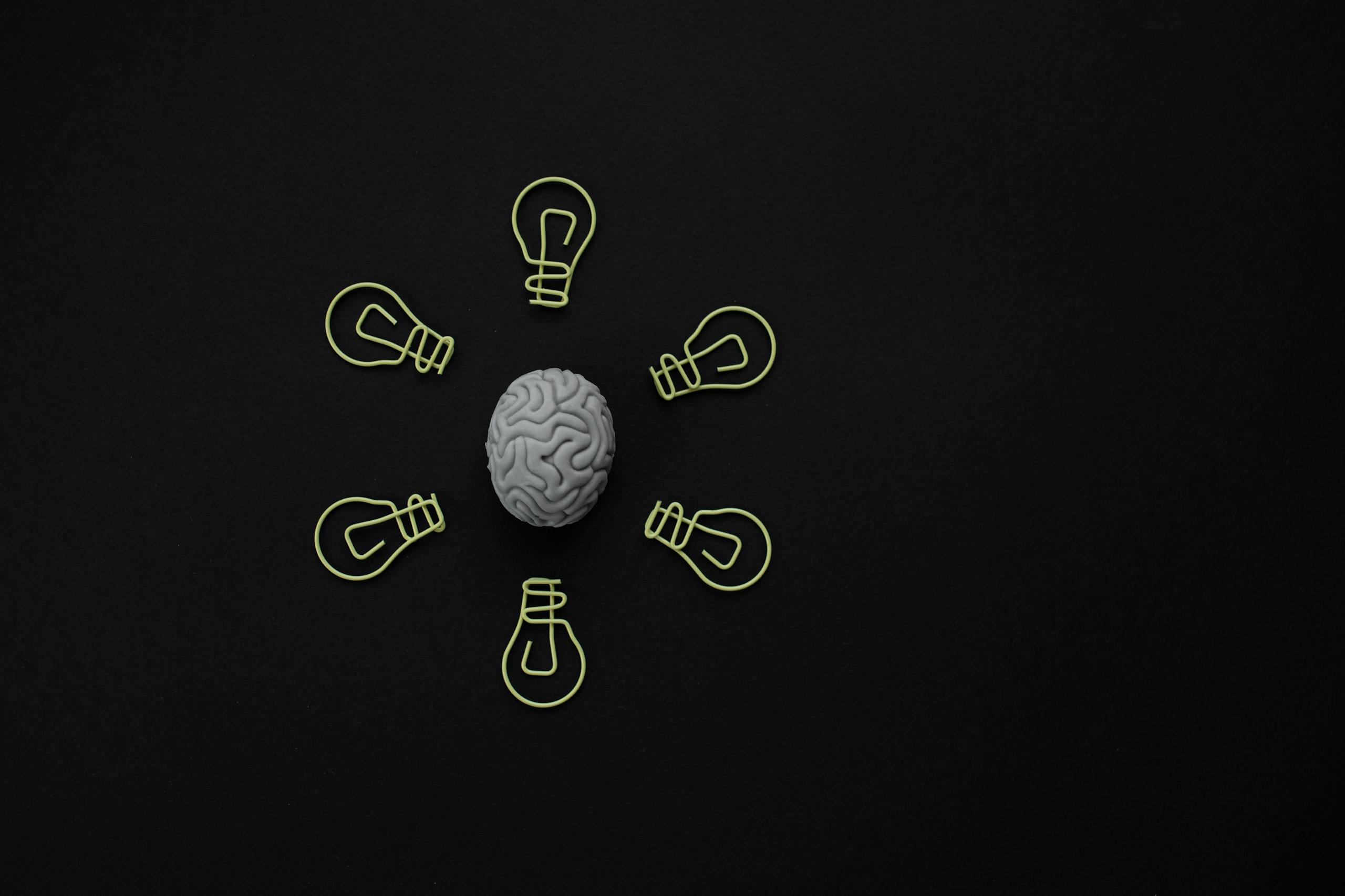 Conceptual photo of a brain surrounded by light bulb clips on black background.
