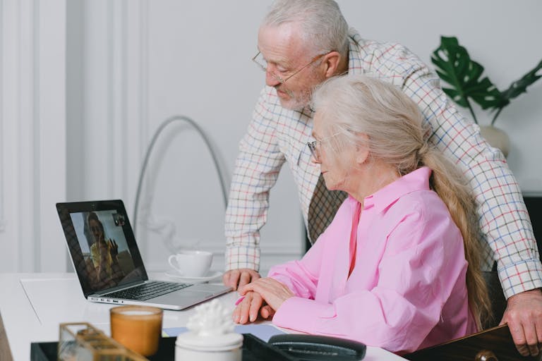 Elderly couple enjoying a video call on their laptop at home, showcasing family connection technology.