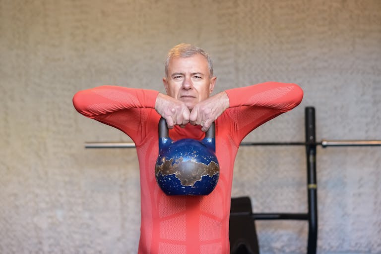 Elderly man engages in strength training with kettlebell, promoting fitness and healthy aging.