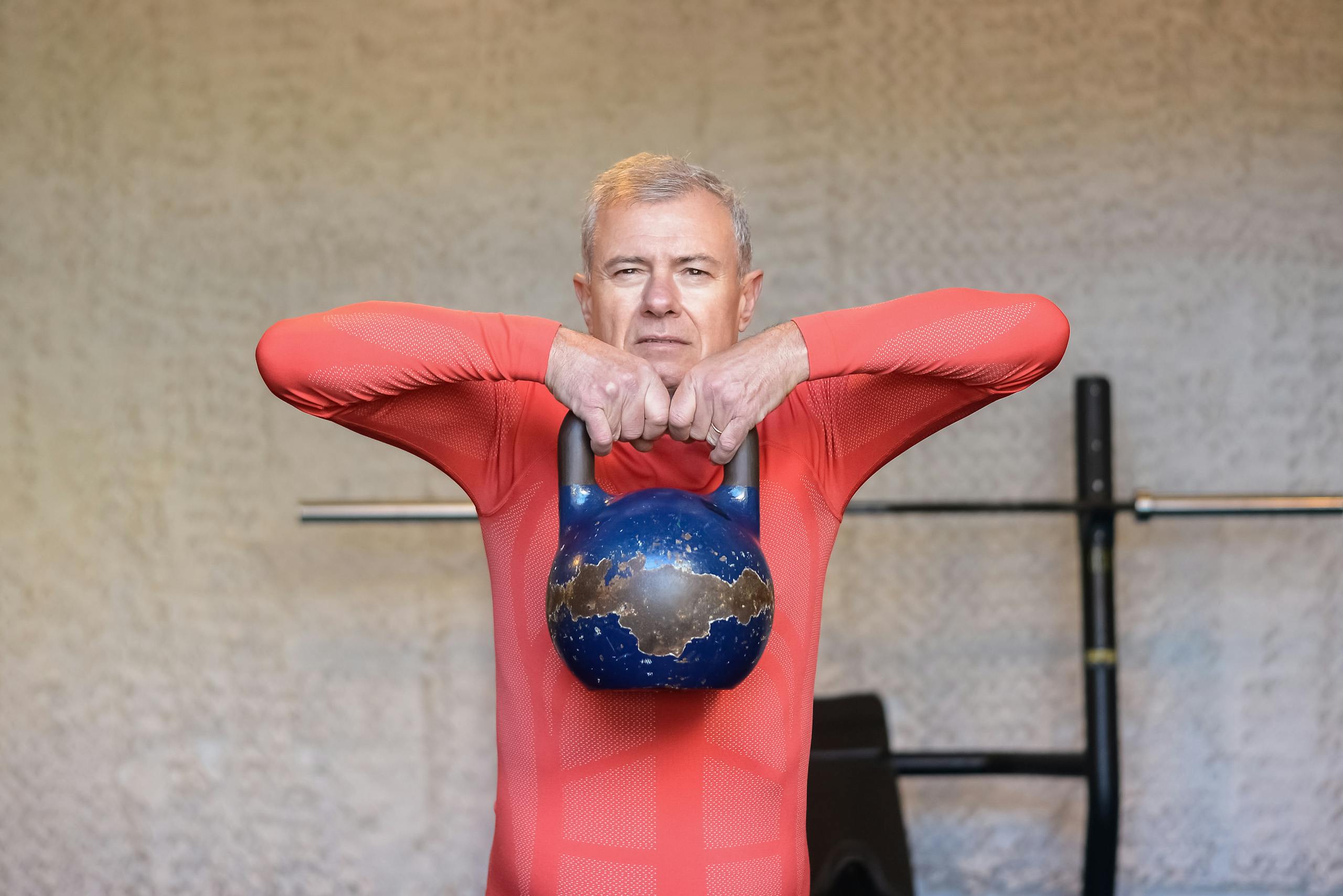 Elderly man engages in strength training with kettlebell, promoting fitness and healthy aging.