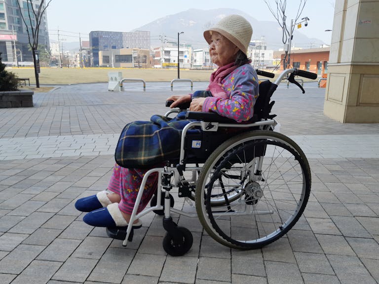Elderly woman sitting in a wheelchair outdoors, showcasing independence and urban life.