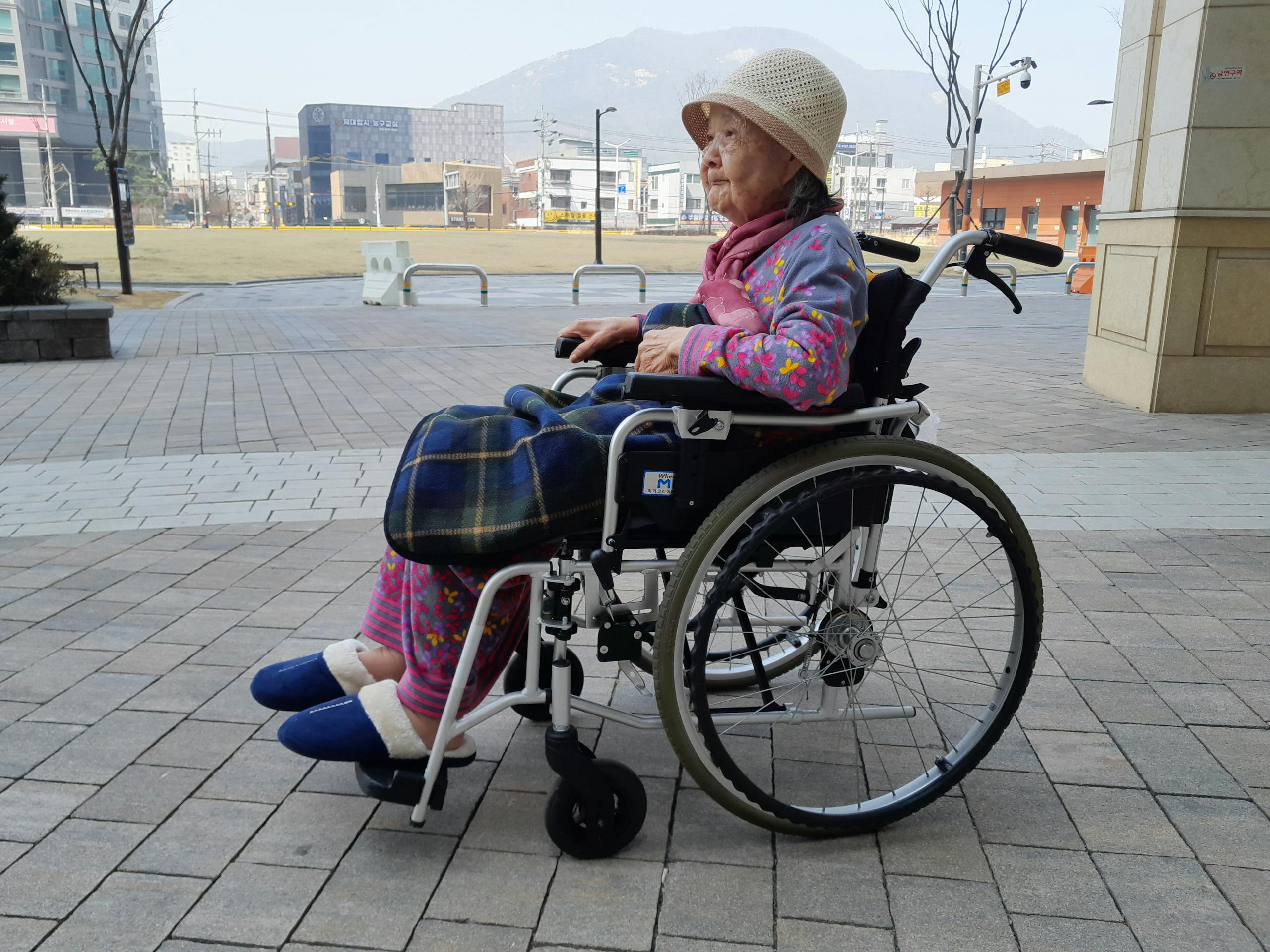 Elderly woman sitting in a wheelchair outdoors, showcasing independence and urban life.