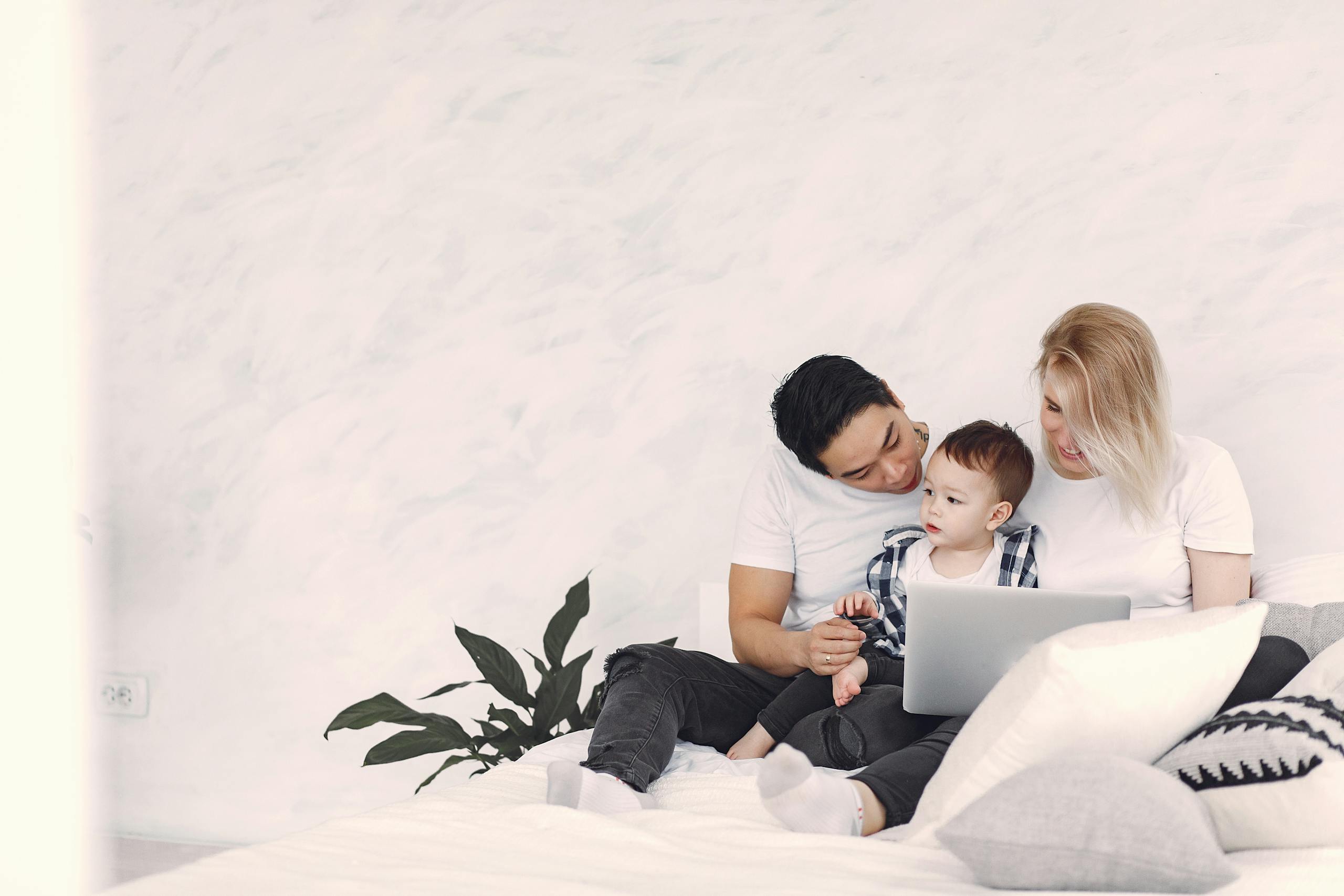 Happy family bonding on bed with laptop in a bright modern bedroom. Perfect for family lifestyle themes.