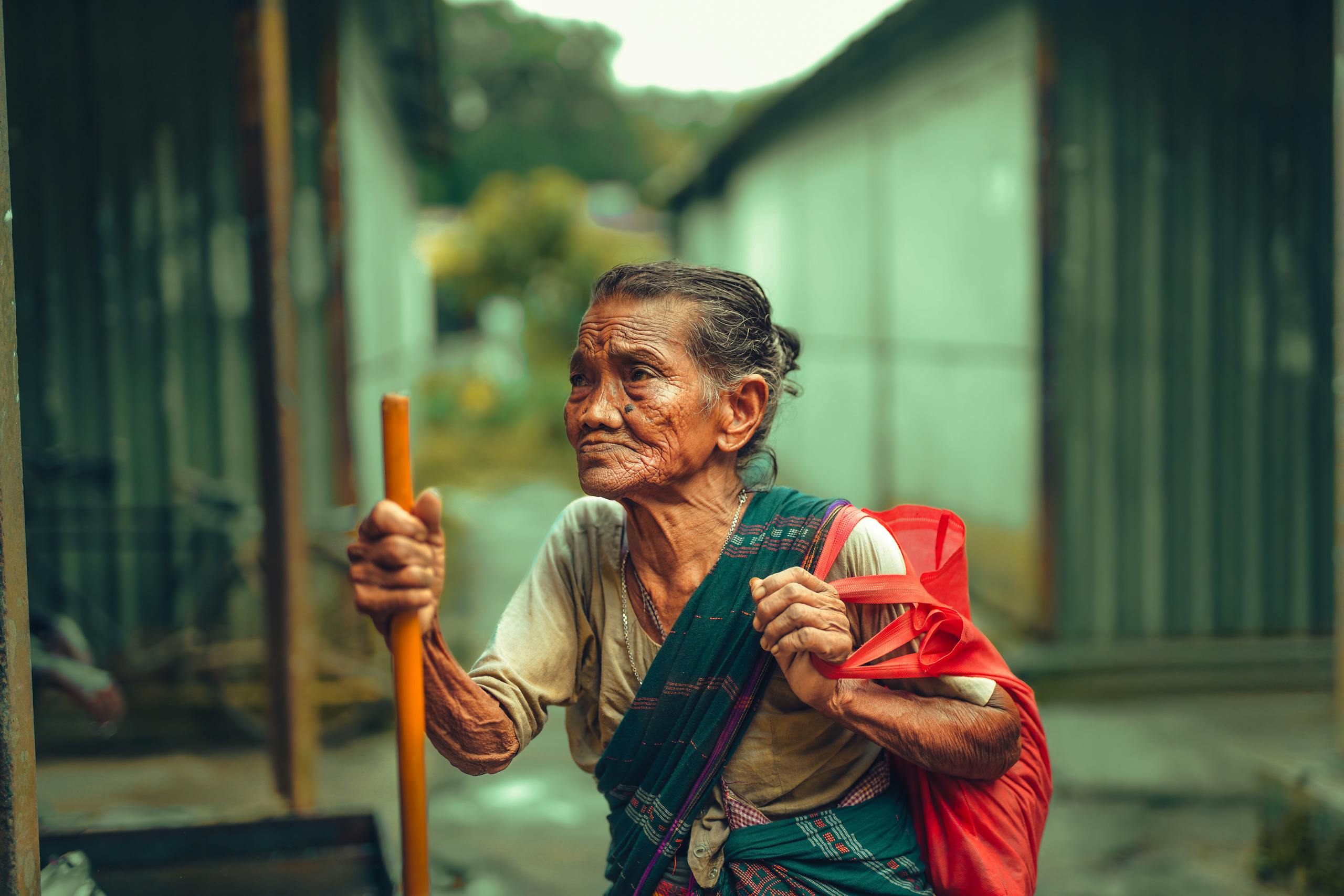Portrait of an elderly woman with a walking stick and bag, captured outdoors.