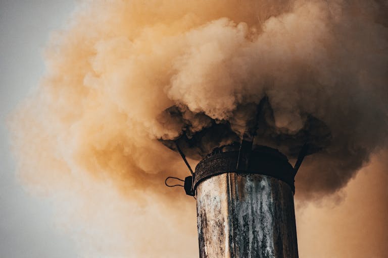 A close-up of a factory smokestack releasing thick smoke into the air, illustrating industrial pollution.