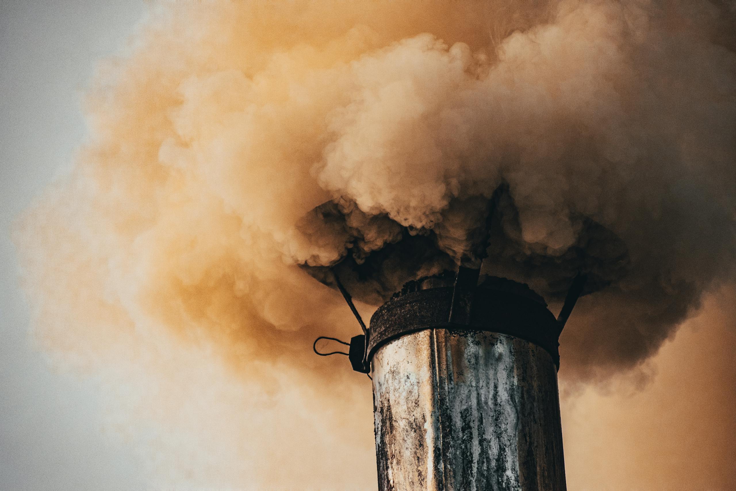 A close-up of a factory smokestack releasing thick smoke into the air, illustrating industrial pollution.