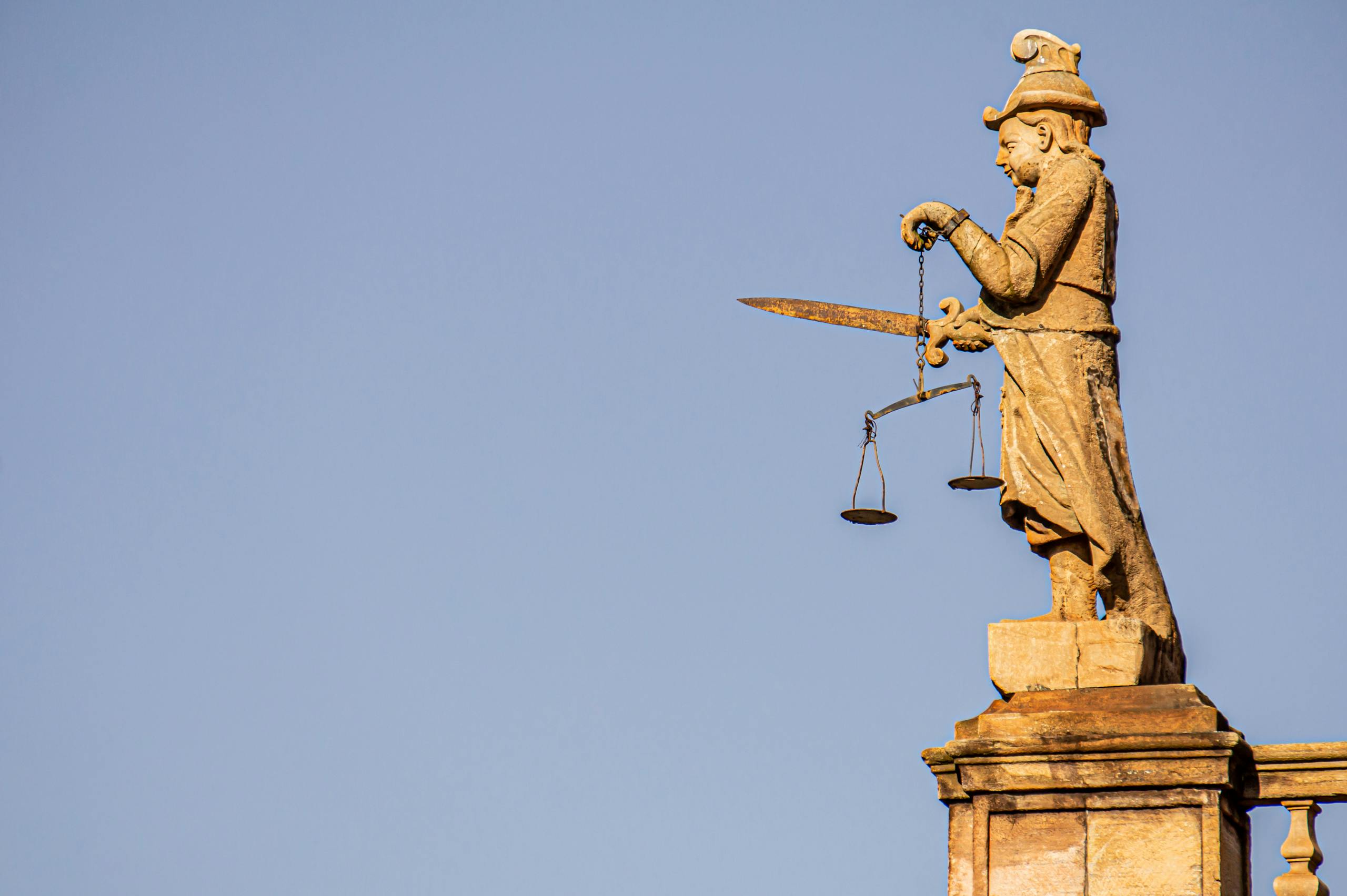 A side view of a justice statue with a sword and weighing scales against blue skies.