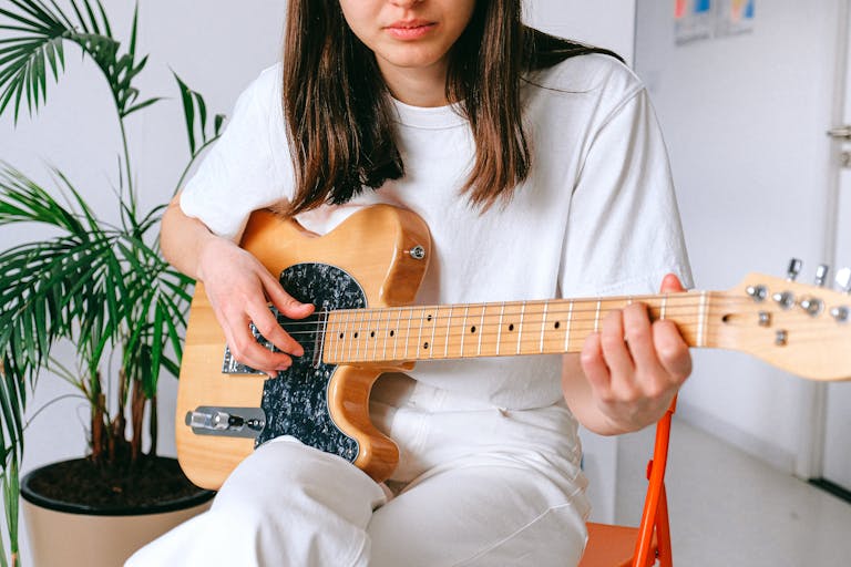 A woman in a white outfit playing an electric guitar indoors, enjoying leisure time.