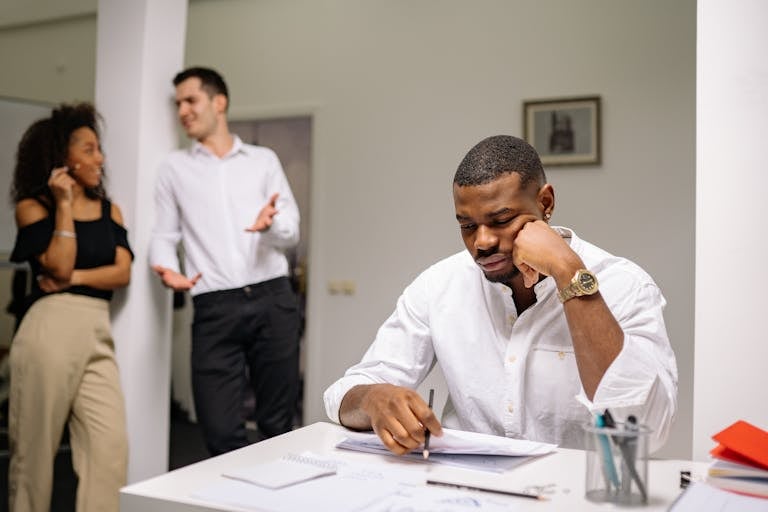 Businessman showing signs of stress surrounded by colleagues in an office environment.