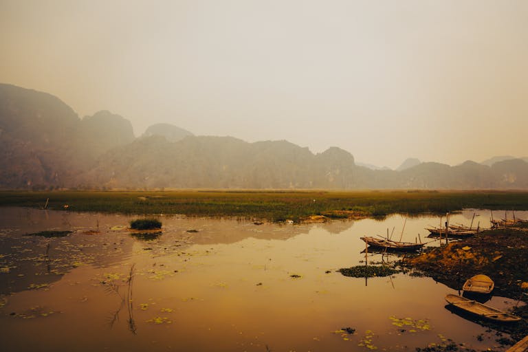Tranquil scene of Ninh Binh river and boats with a mountainous backdrop at twilight.